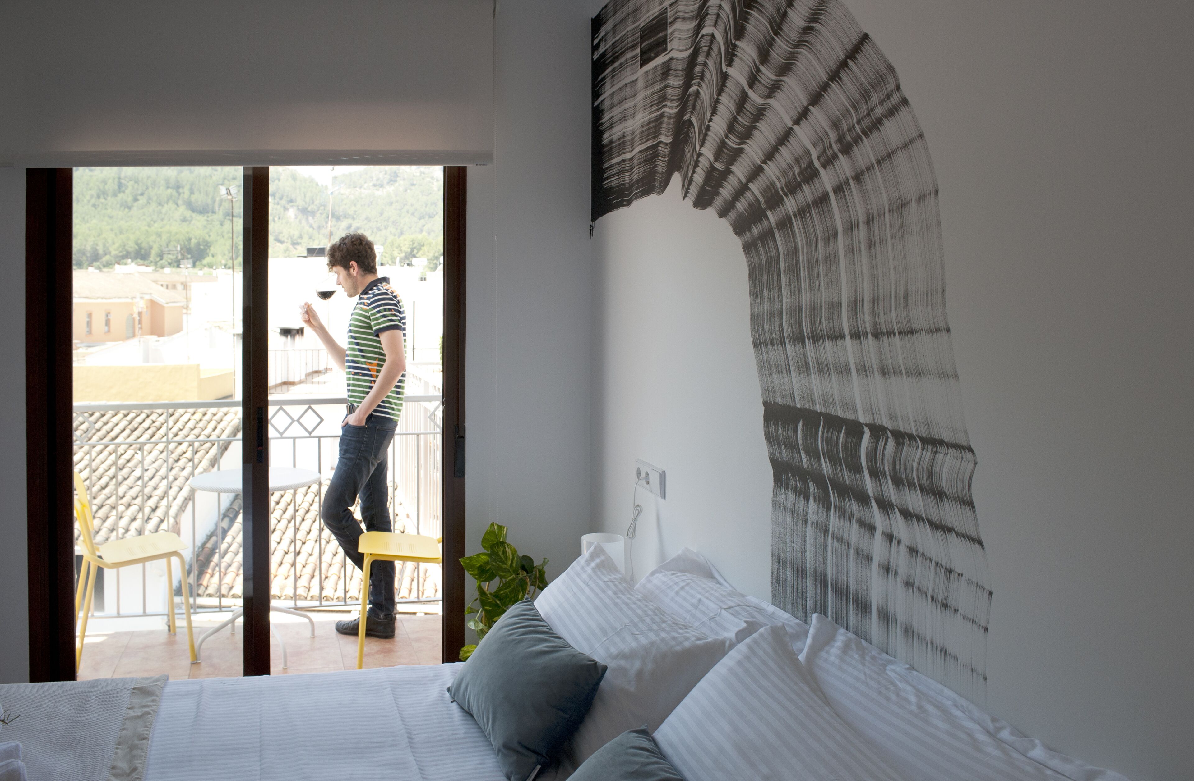 Un dormitorio con cama, ventana, balcón y pared decorada con una obra de arte texturizada.
