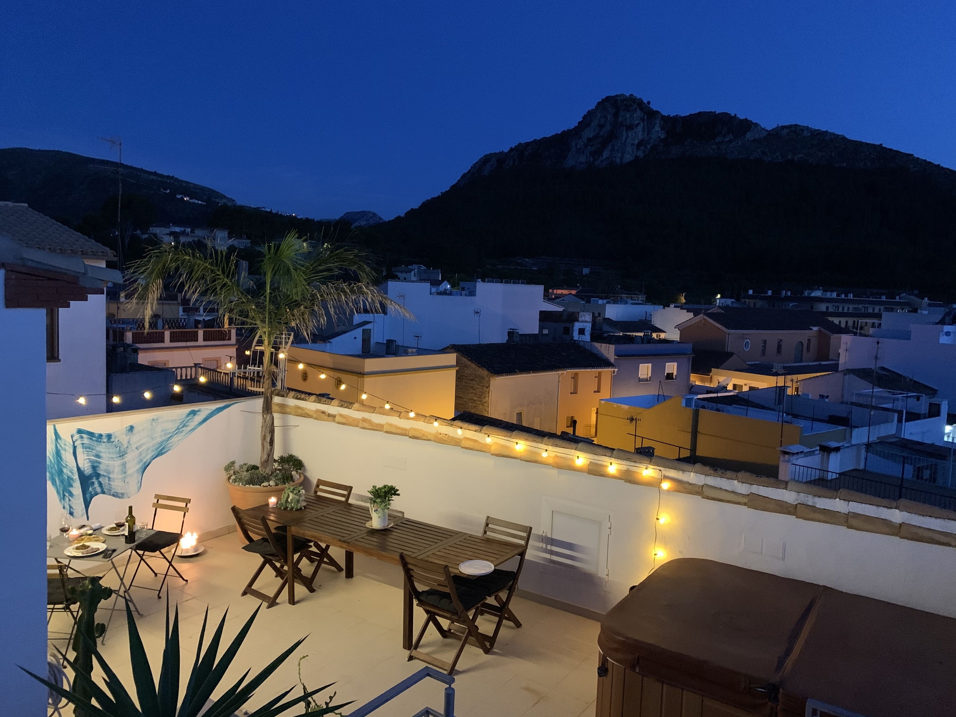 A rooftop terrace with a dining table and chairs, surrounded by string lights.