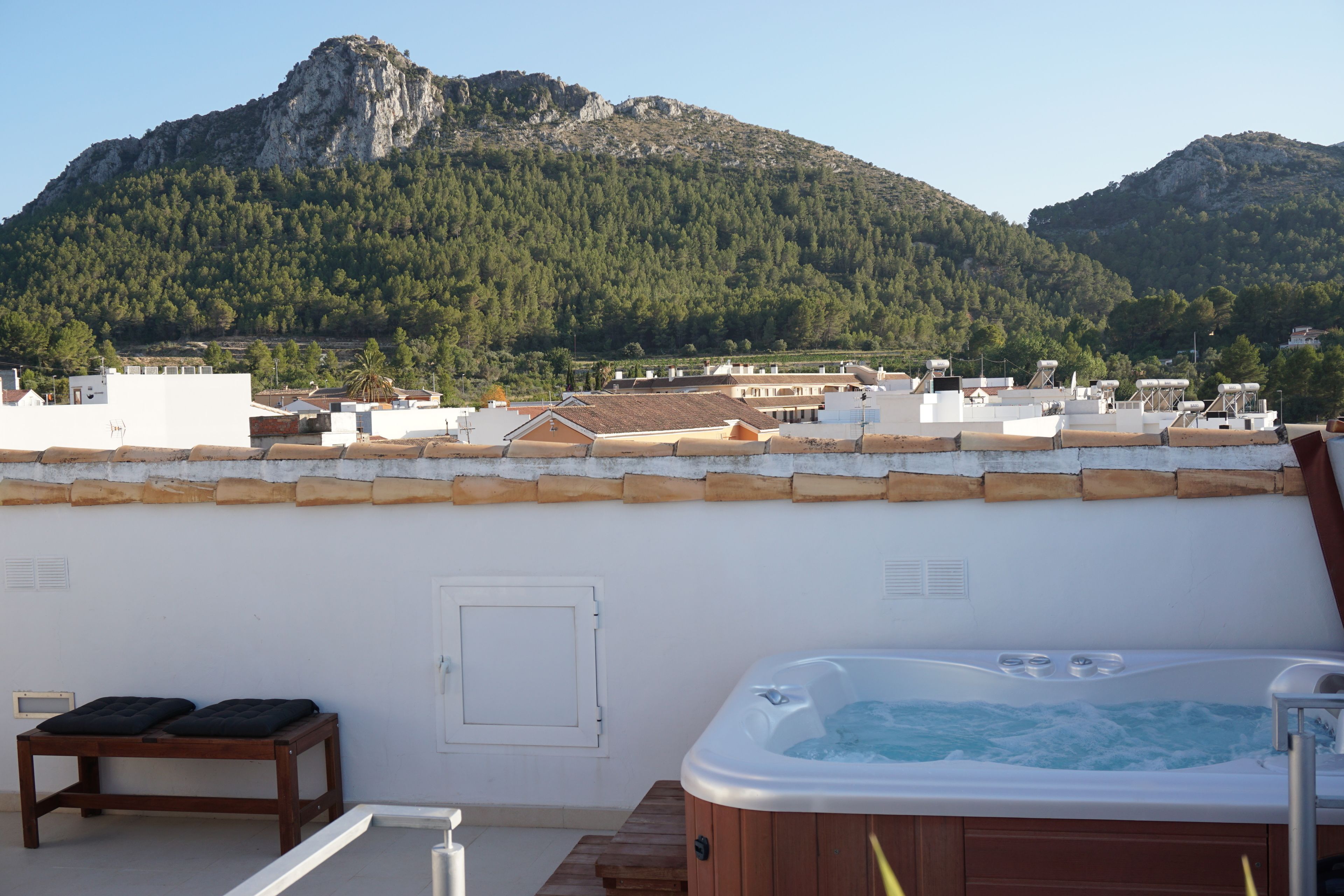 A rooftop with a hot tub, a wooden bench, and a view of a mountainous landscape.