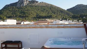 A rooftop with a hot tub, a wooden bench, and a view of a mountainous landscape.