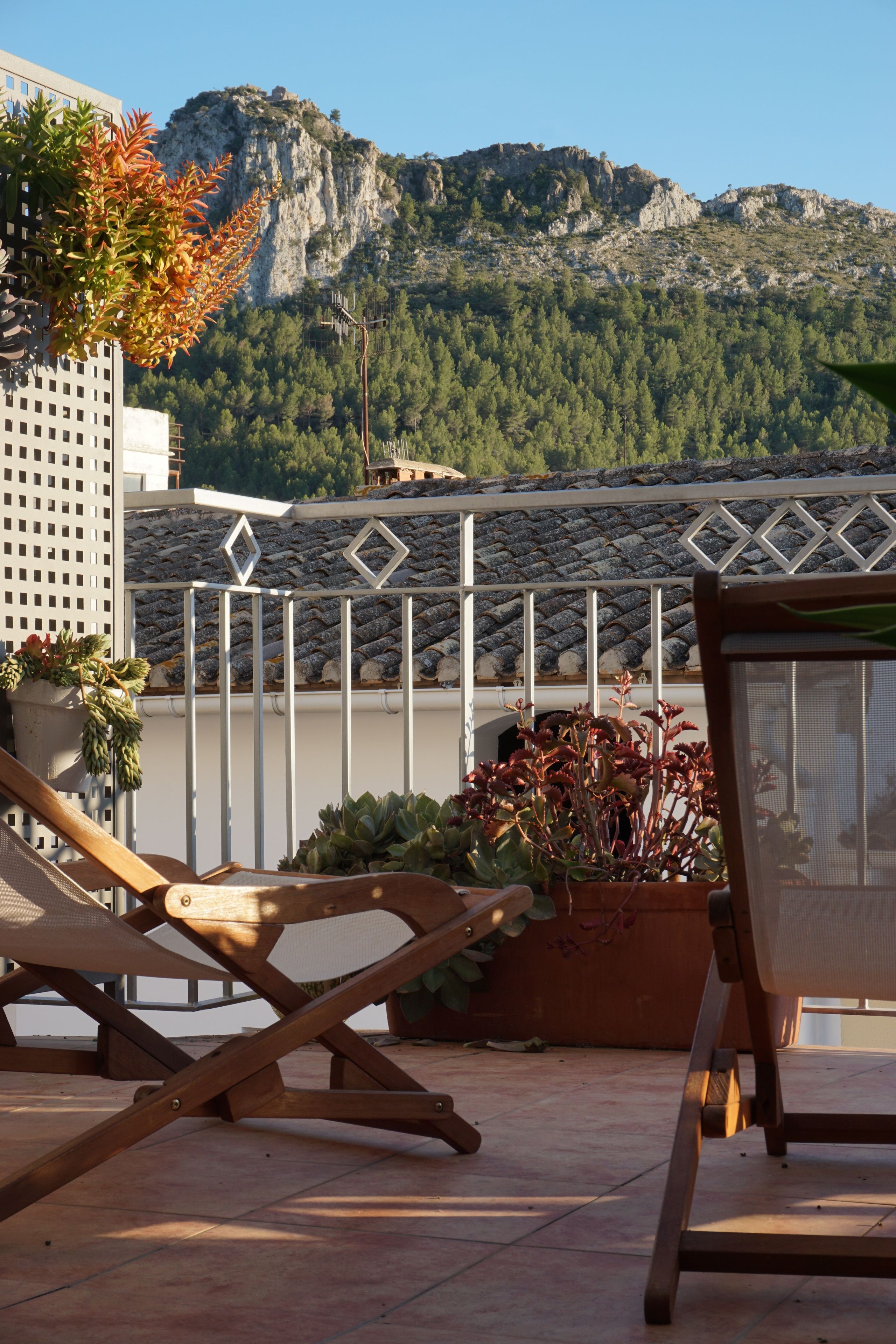 A terrace with wooden chairs and a potted plant, overlooking a mountainous landscape.