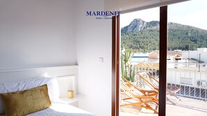 Ein Schlafzimmer mit einem Bett, einem Nachttisch und Blick auf einen Balkon mit Gartenmöbeln.