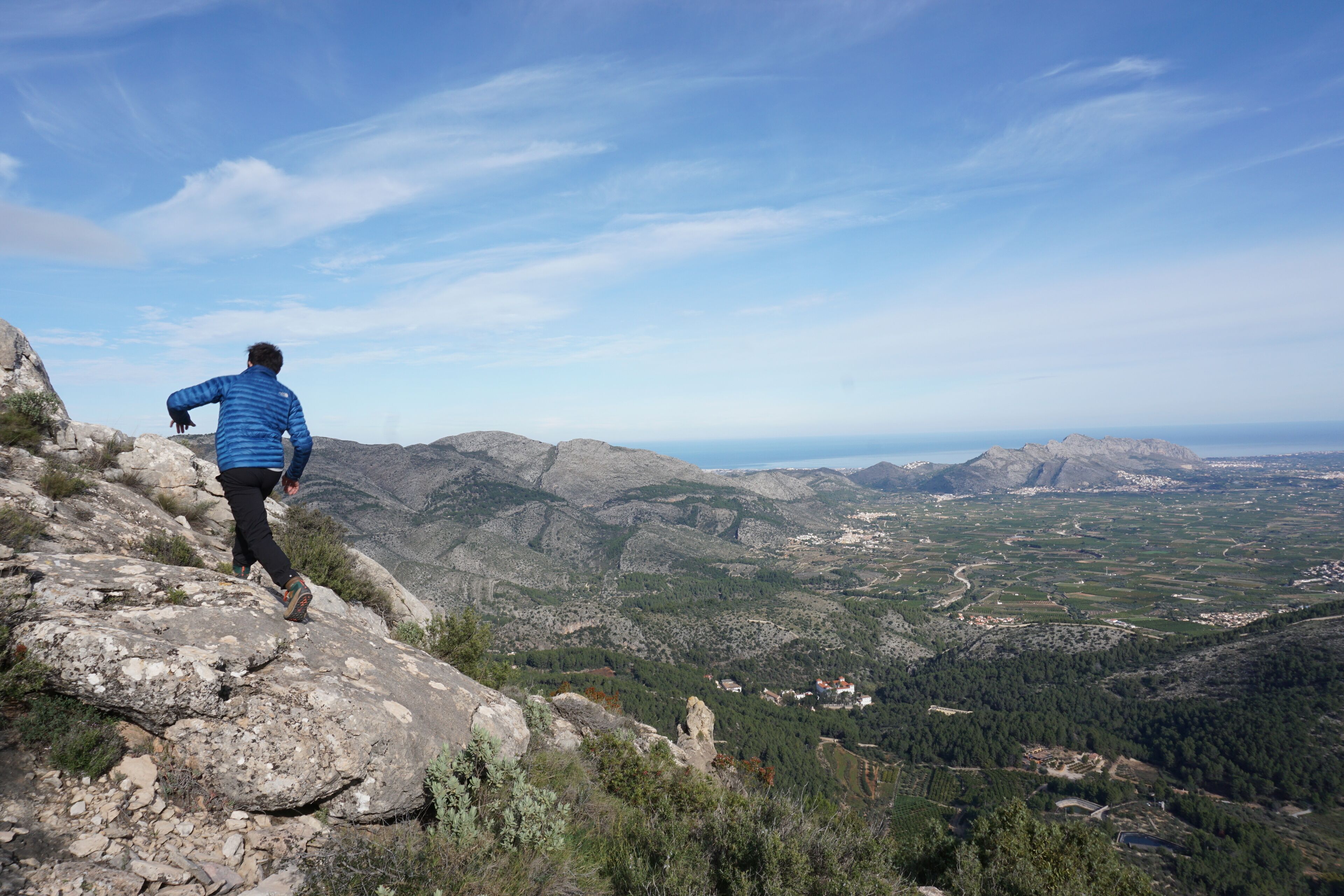 A person hiking on a rocky path with a view of a valley and distant mountains.