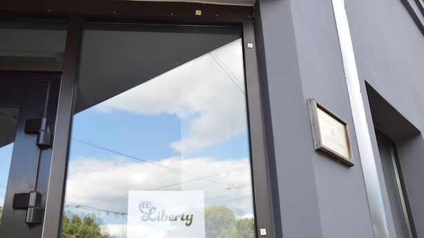 A building entrance with a glass door reflecting the sky and trees. - Liberty Airy (Riga)