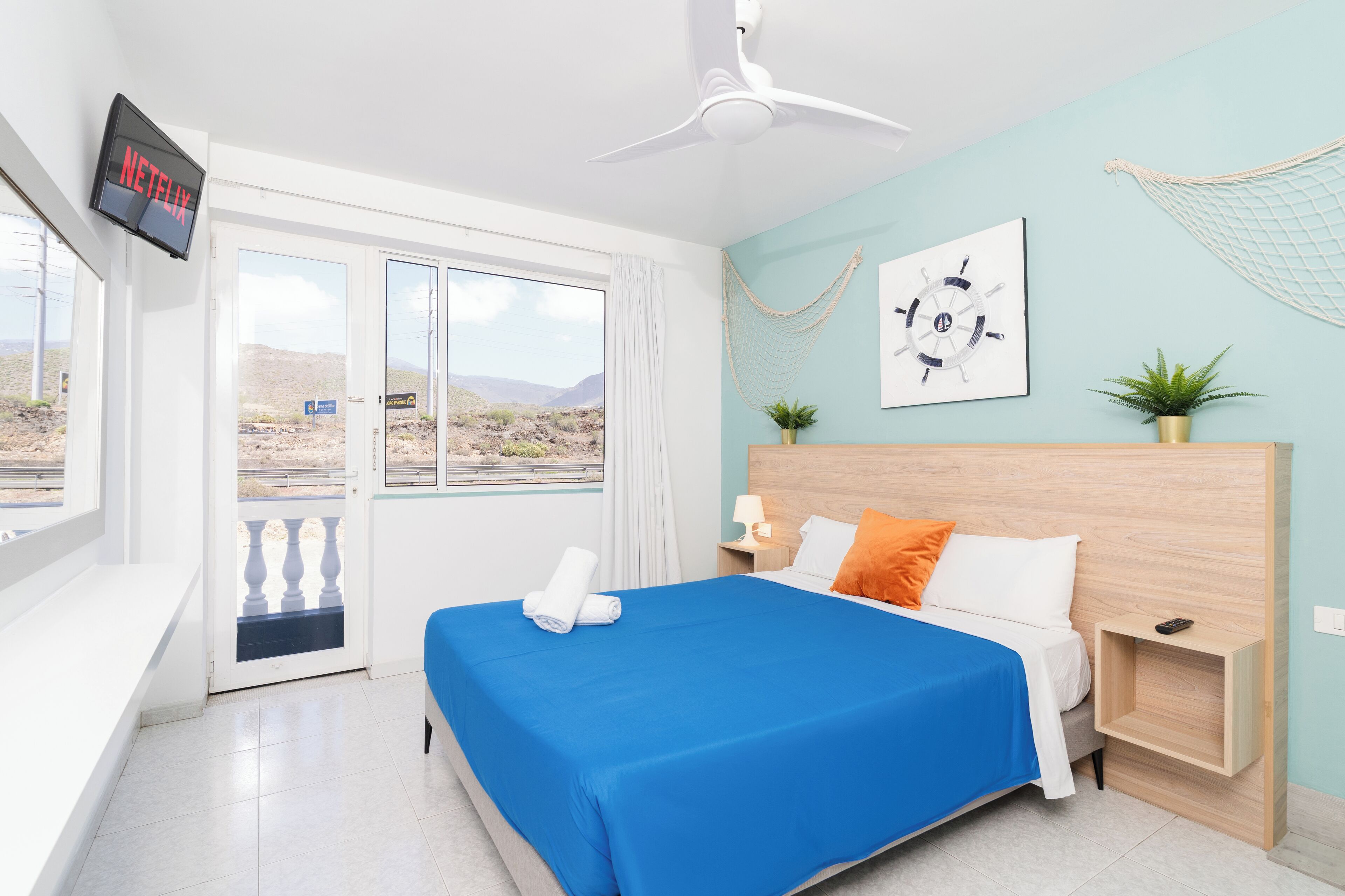 Habitación de hotel con cama, televisión, ventana con vistas al desierto y ventilador de techo.