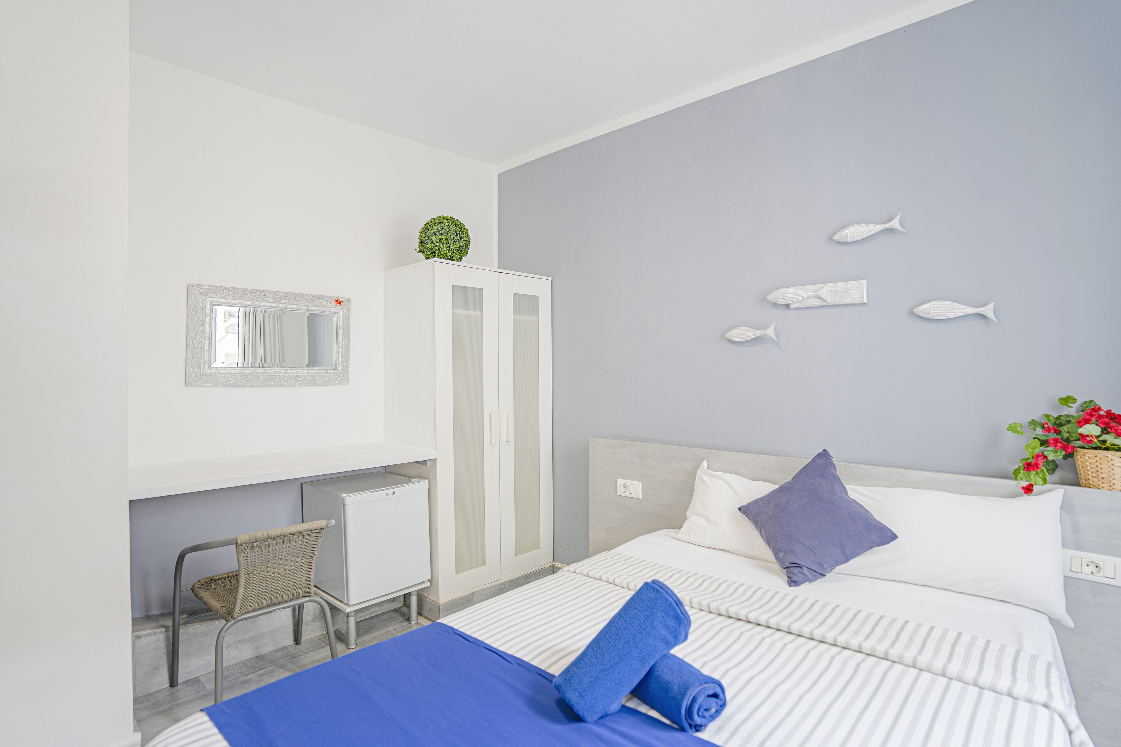 Habitación de hotel con cama, escritorio, silla, armario y una pared decorada con motivos de peces.