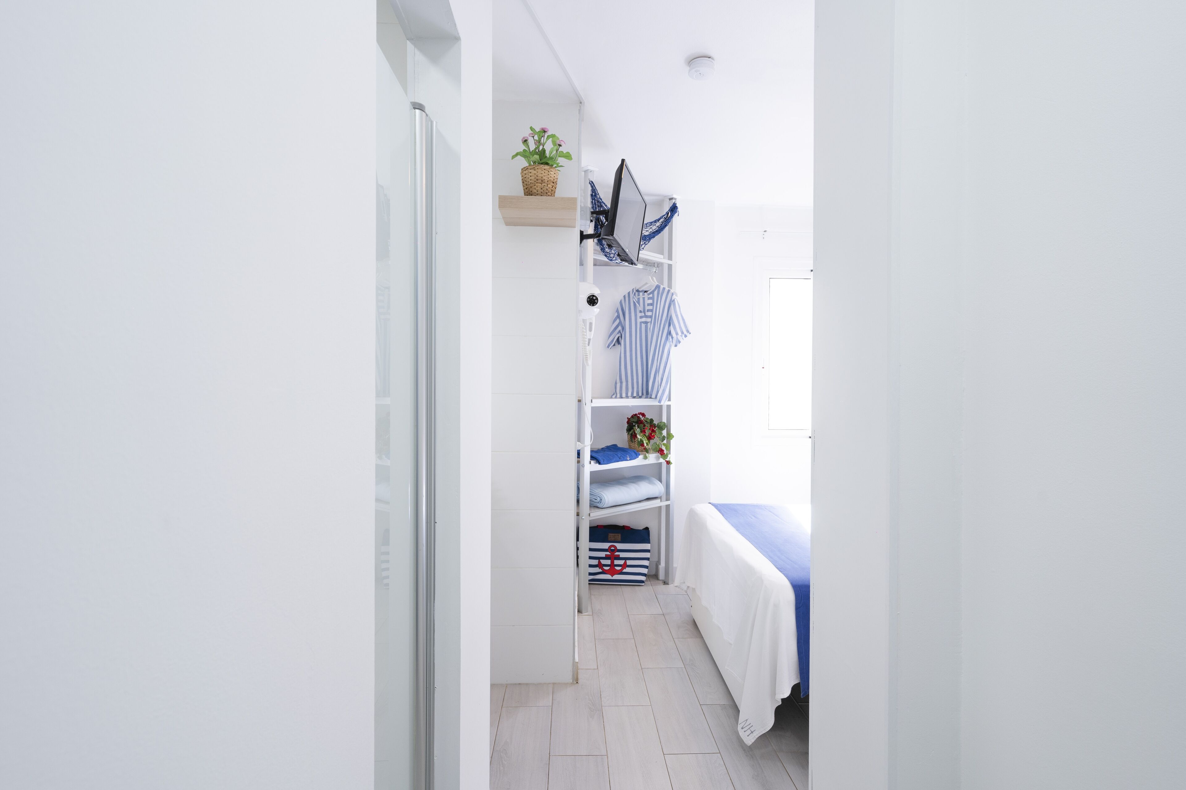 A narrow room with a bed, a shelf with folded clothes, and a small plant.