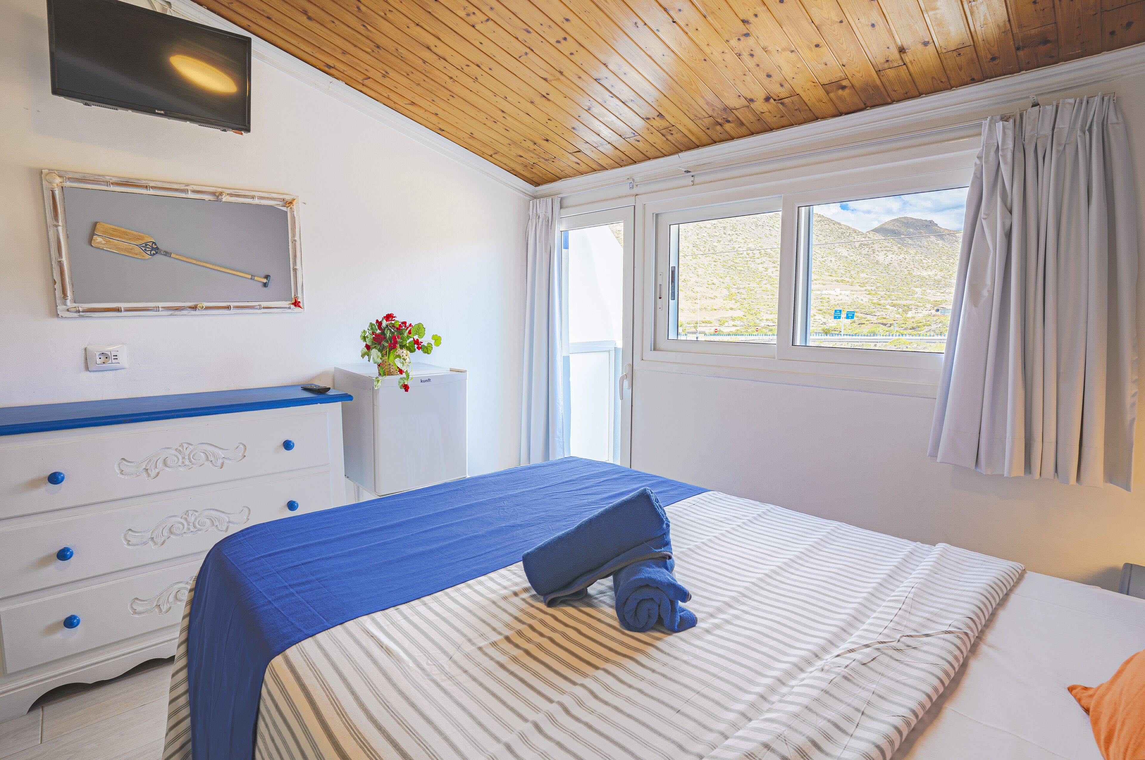 A bedroom with a bed, a dresser, a TV, and a window with curtains.