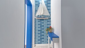 A hallway with a blue brick wall, a white sailboat decoration, and a blue bench with a basket of flowers.