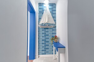 Un pasillo con una pared de ladrillo azul, un adorno de velero blanco y un banco azul con una cesta de flores.