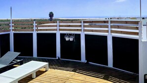 A wooden deck with a white railing, a palm tree, and a view of the ocean.