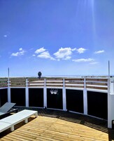 Una terraza de madera con barandilla blanca, una palmera y vista al océano.
