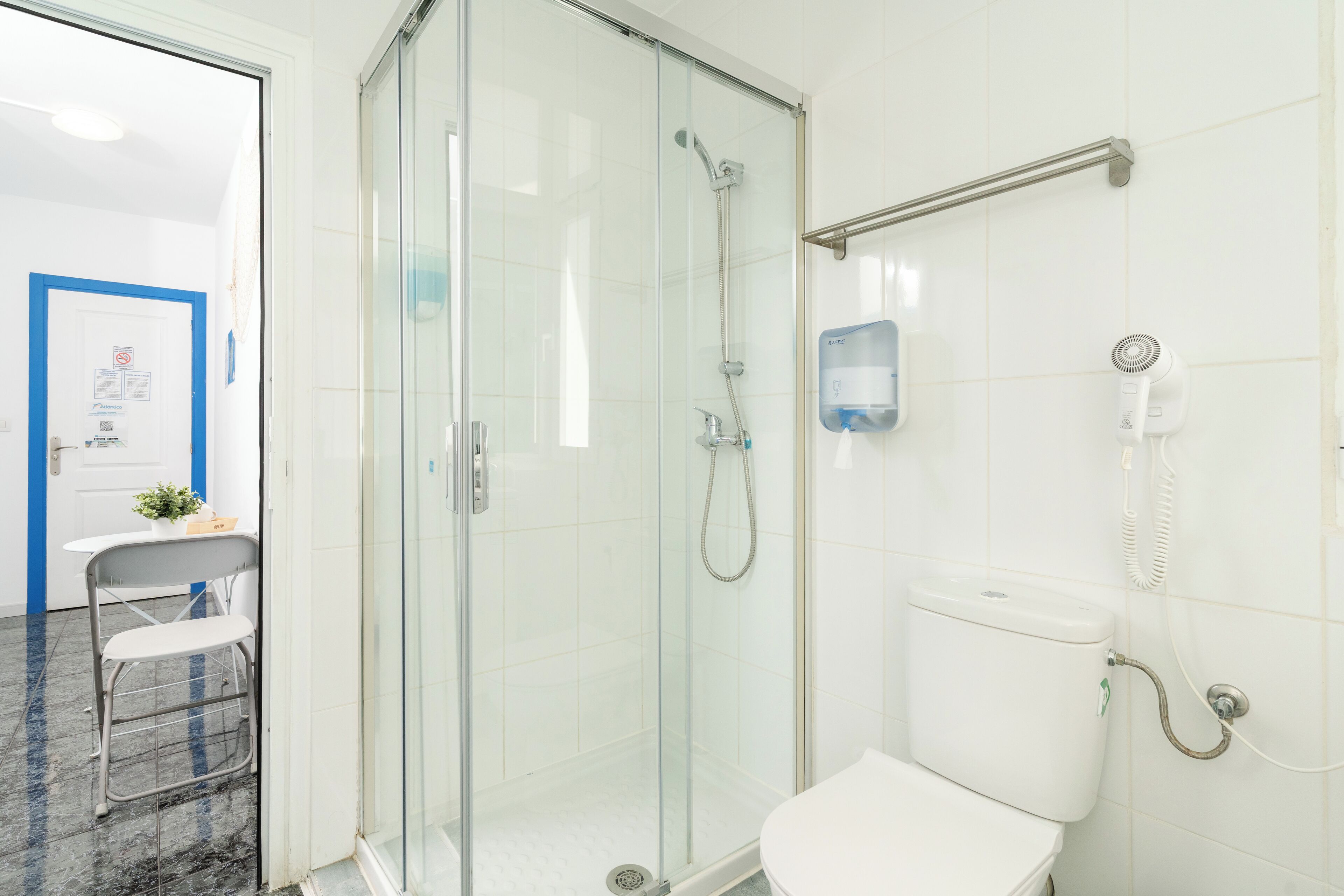 A bathroom with a glass-enclosed shower, a toilet, and a hand dryer mounted on the wall.