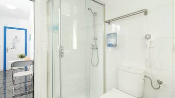 A bathroom with a glass-enclosed shower, a toilet, and a hand dryer mounted on the wall.