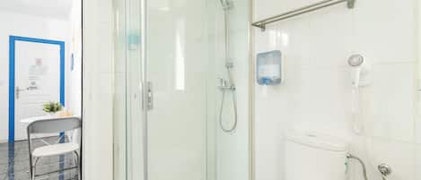 A bathroom with a glass-enclosed shower, a toilet, and a hand dryer mounted on the wall.