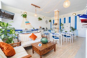 Una sala de estar moderna con un sofá, una mesa de centro y un comedor. Se ve una cocina al fondo, con una encimera y sillas.
