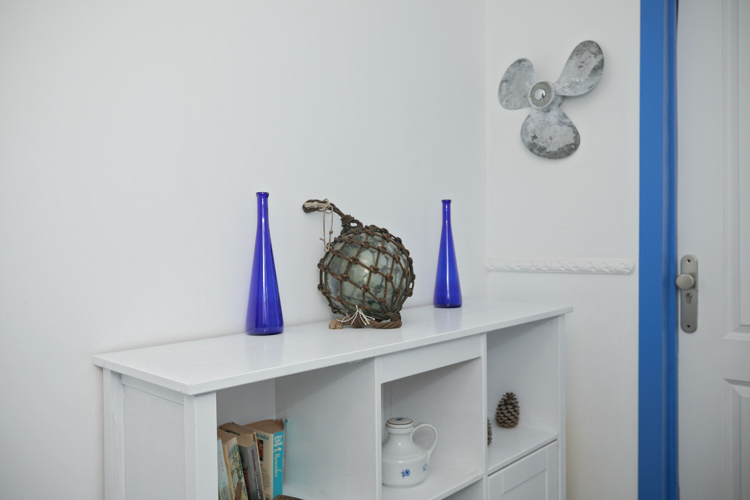 Een witte console tafel met twee blauwe vazen, een decoratieve bol en een wandventilator.