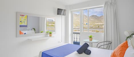 Habitación de hotel con cama, televisión, ventana con vistas a las montañas y una pequeña mesa con una planta.
