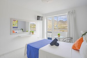 Habitación de hotel con cama, televisión, ventana con vistas a las montañas y una pequeña mesa con una planta.