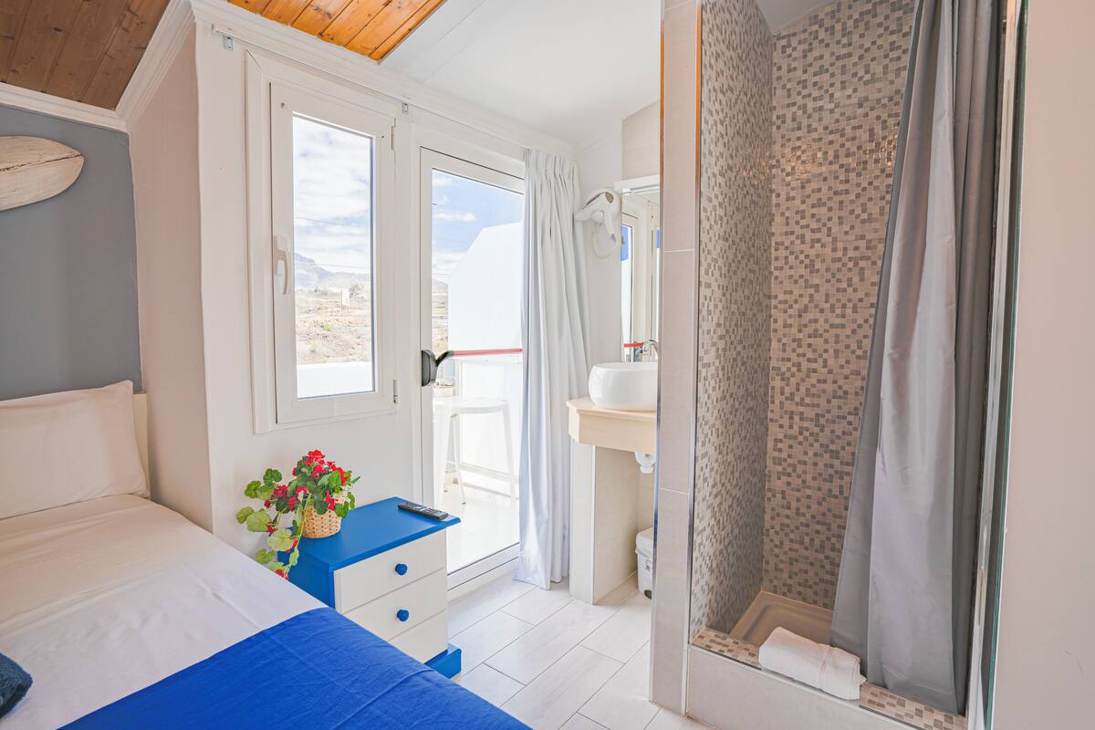 Quarto com cama, mesa de cabeceira com controle remoto e janela com vista.