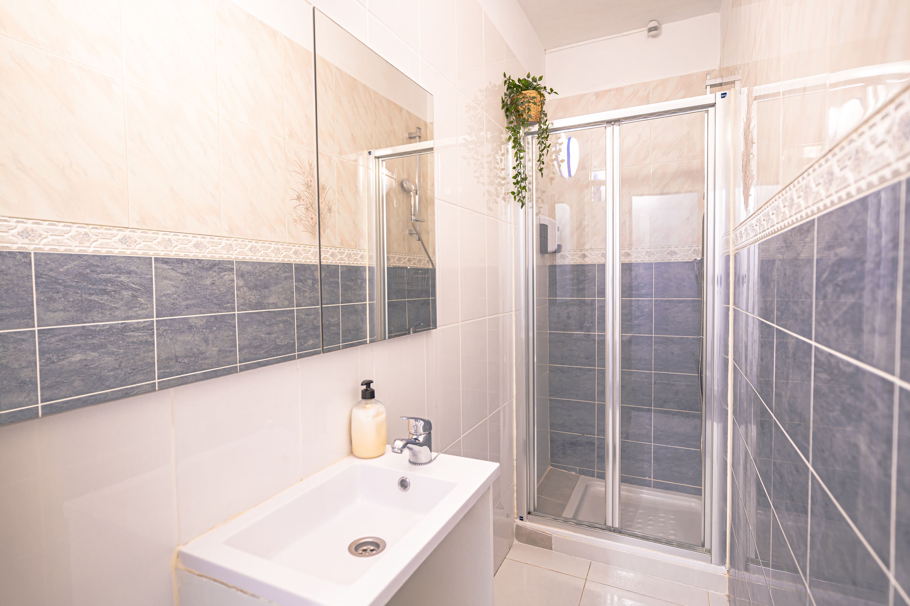Une salle de bain moderne avec un lavabo blanc, une douche en verre et un miroir orné d’une bordure de carreaux décoratifs.