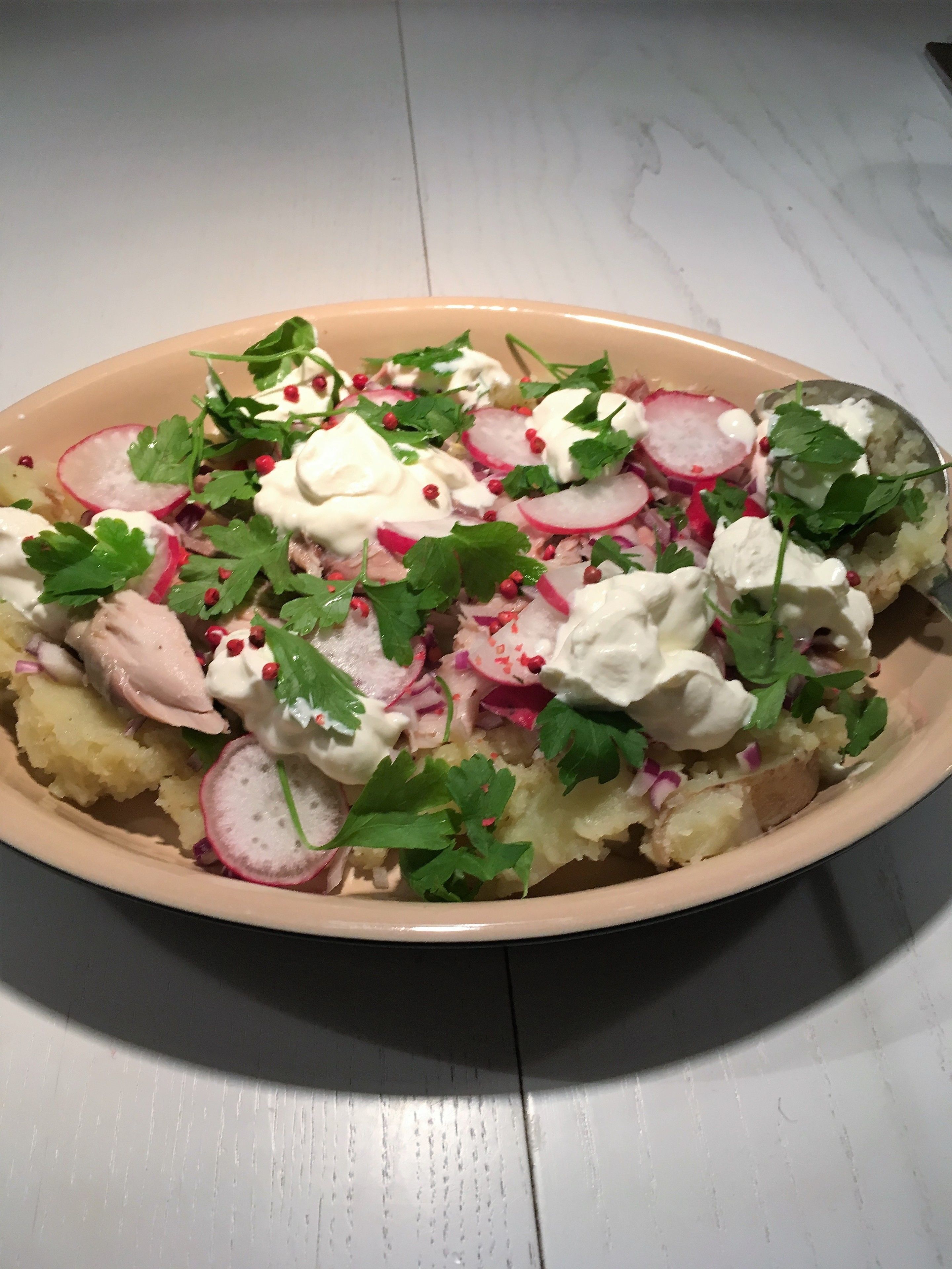 Een schaal eten met diverse toppings, zoals radijsjes, kruiden en een romige saus.