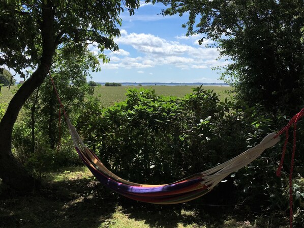 A hammock in a lush garden with a view of a field and distant horizon.