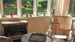 A sunlit patio with wicker furniture, a small table, and a window overlooking a garden.