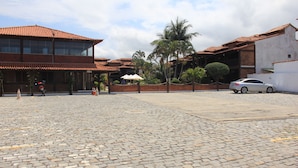 A courtyard with cobblestone paving, palm trees, and a car parked in the background.