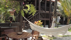 An outdoor patio with a wooden table and chairs, a hammock, and a variety of plants.