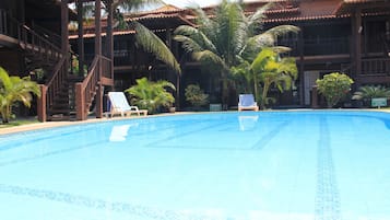 A swimming pool with lounge chairs, palm trees, and a building with a tiled roof.