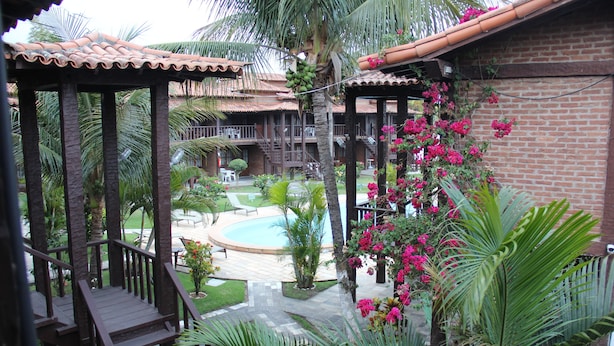 A pool area with a wooden deck, palm trees, and a brick building with a tiled roof.