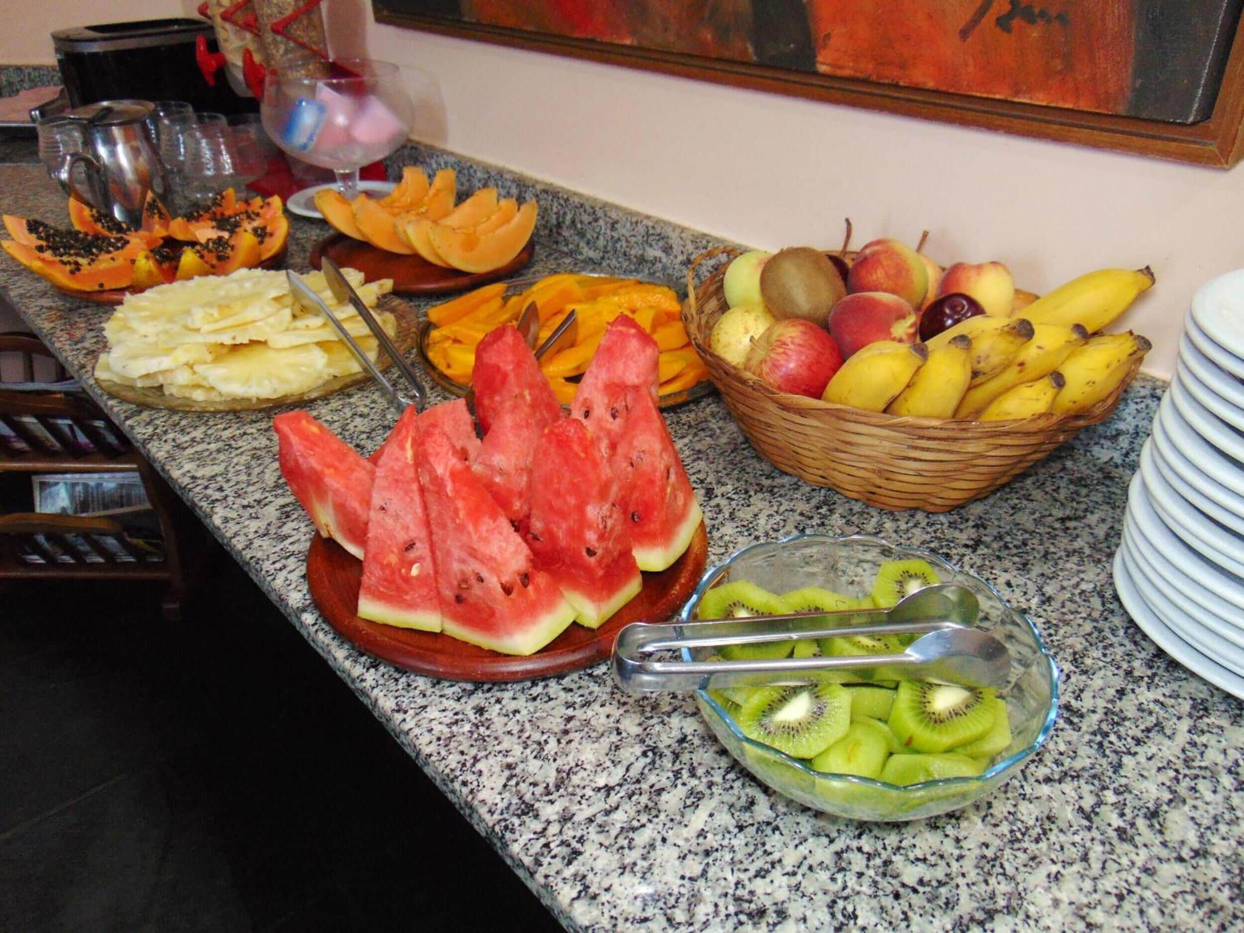 Uma tábua de frutas com melancia, kiwi e outras frutas diversas sobre uma bancada de cozinha.
