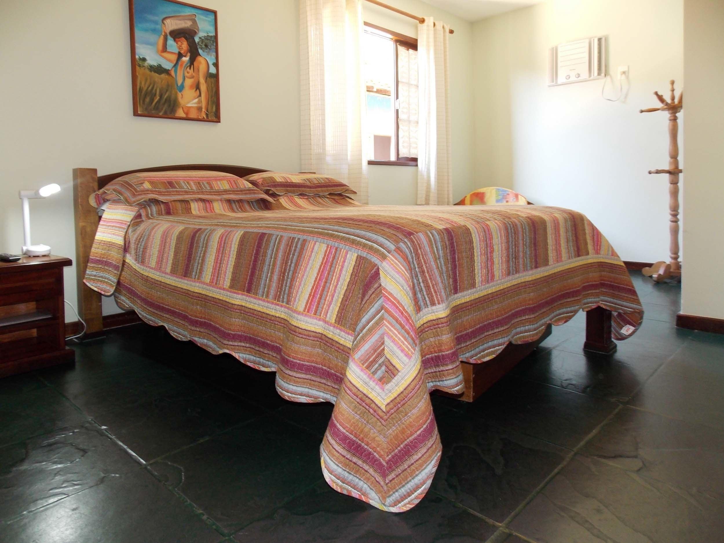 A bed with a striped blanket, a bedside lamp, and a painting on the wall.