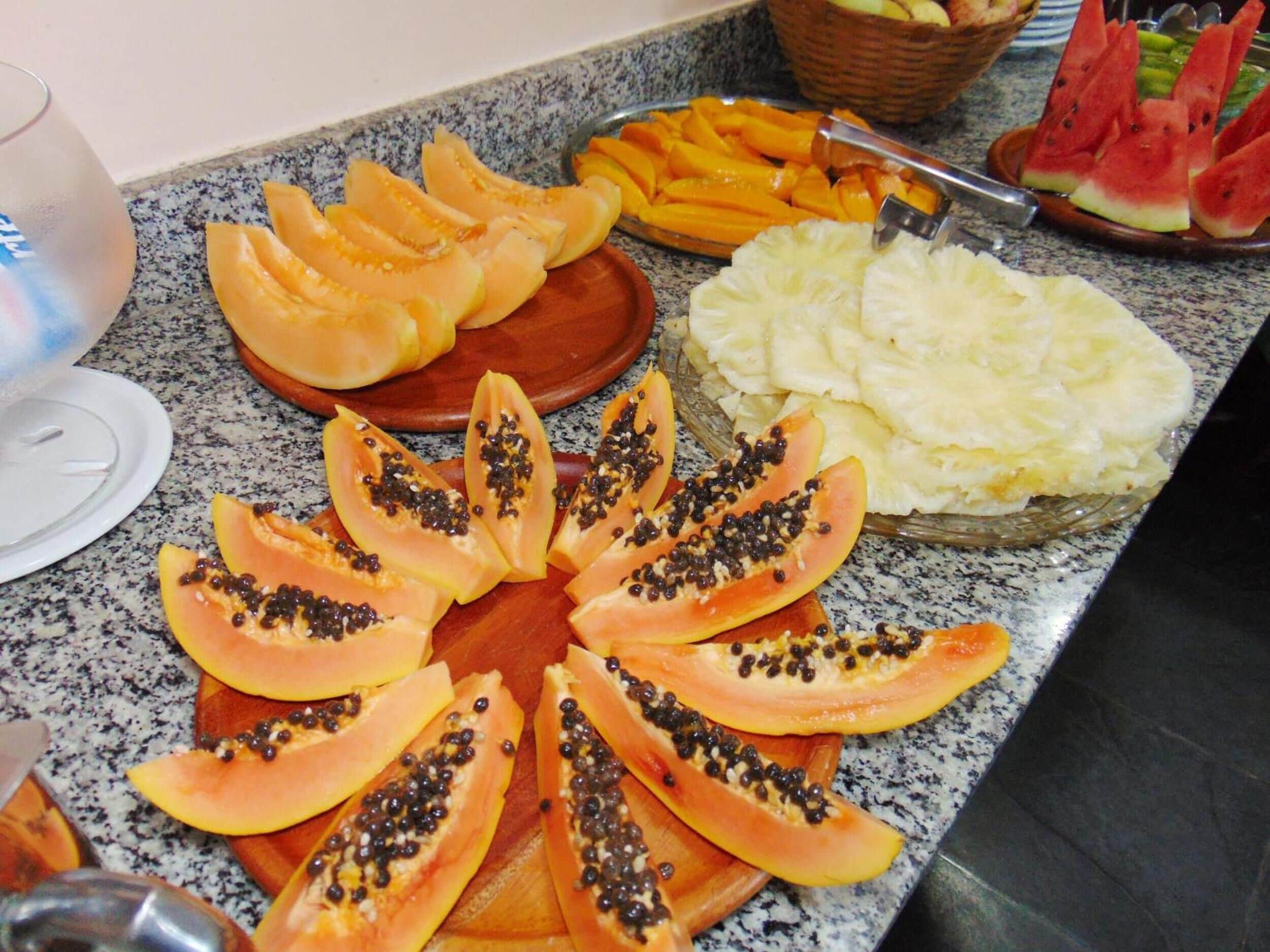 Obstteller mit Papaya-, Mango- und Ananasscheiben auf einer Granit-Arbeitsplatte.