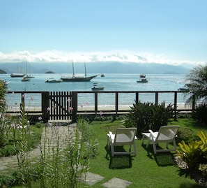A patio with two white lounge chairs, a wooden fence, and a view of the sea with several boats. - Pousada Ancoradouro (Angra dos Reis)