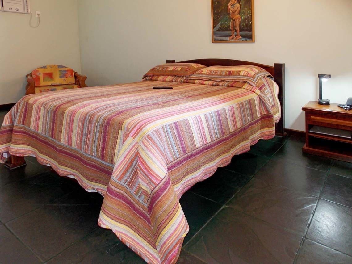 A bed with a striped bedspread, a chair, a nightstand, and a painting on the wall.