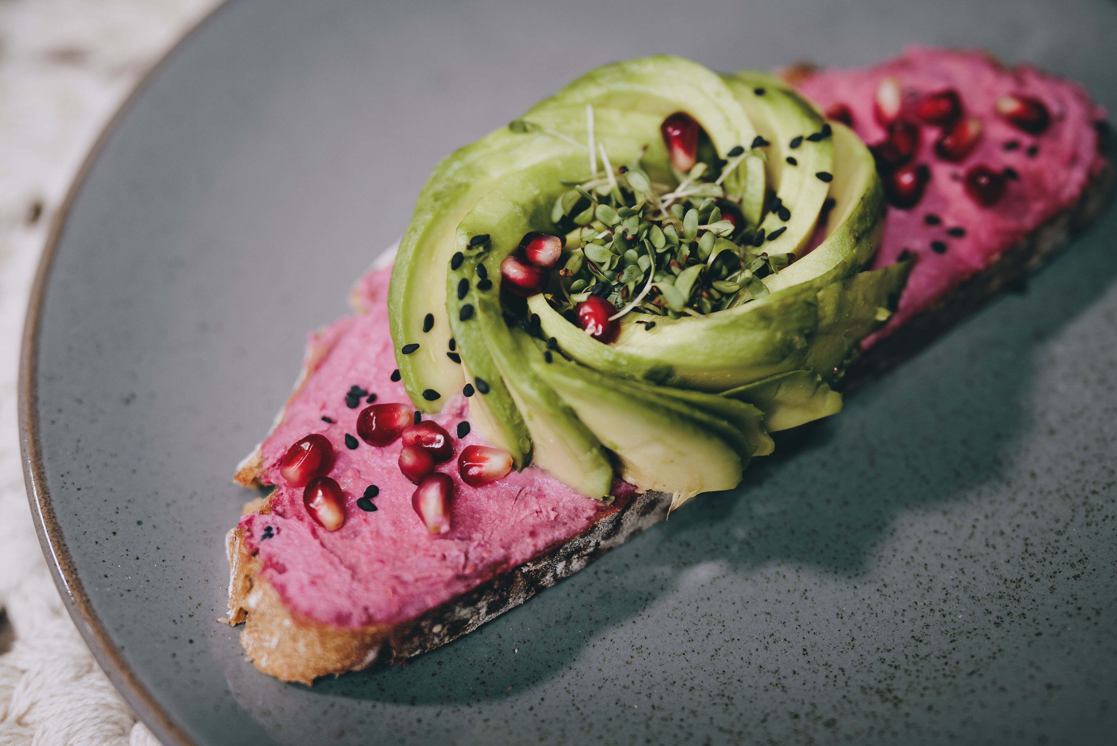 Une assiette avec une tranche de viande, garnie d’avocat, de graines de grenade et de jeunes pousses.