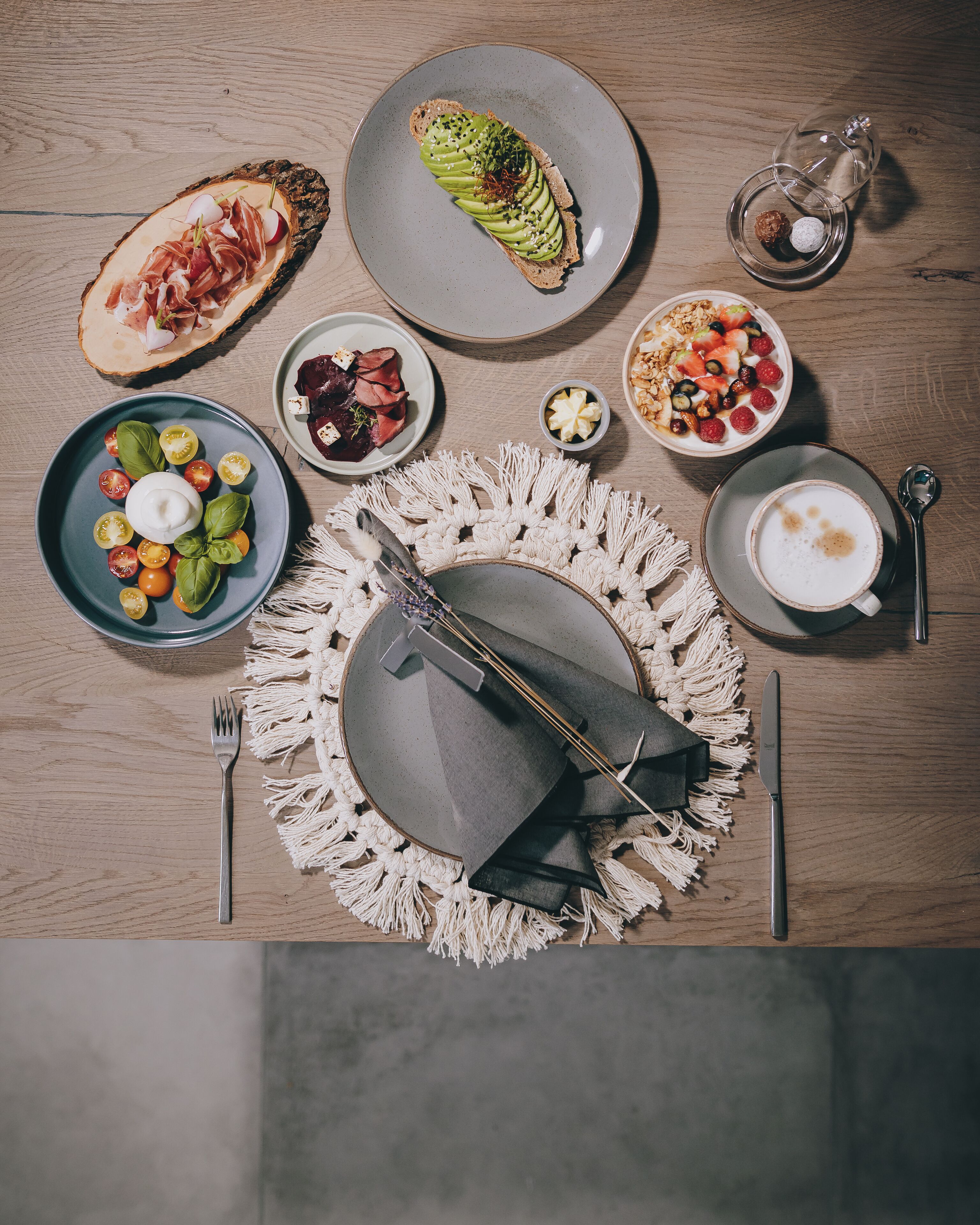 Een gedekte tafel met diverse gerechten, waaronder parmaham, een saladekom, een kop koffie en een decoratief middelpunt.