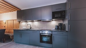 A modern kitchen with grey cabinets, a built-in oven, a microwave, and a coffee maker. - Margarethenstein Boutique Hotel & Apartment (Kaprun)