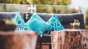A sofa with patterned cushions and a small plant, set against a blurred outdoor background. - Margarethenstein Boutique Hotel & Apartment (Kaprun)