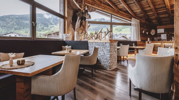 A rustic interior with wooden beams, a stone fireplace, and a large deer head mounted on the wall. Tables and chairs are arranged for dining. - Margarethenstein Boutique Hotel & Apartment (Kaprun)