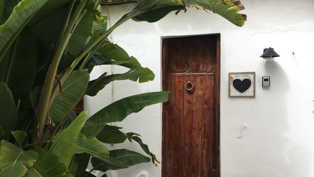 A wooden door with a metal knocker, a white wall, and a welcome sign with a heart. - La Casita de Las Palmas VV (Las Palmas de Gran Canaria)