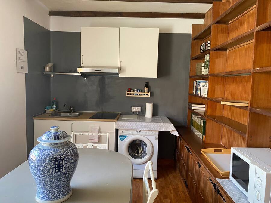 Una cocina funcional con lavadora, microondas y una estantería de madera.