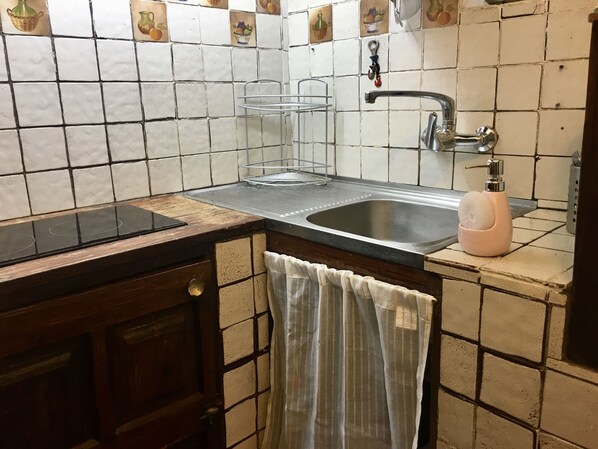 Una cocina con un lavamanos de acero inoxidable, un escurreplatos metálico, un dispensador de jabón y un armario de madera.