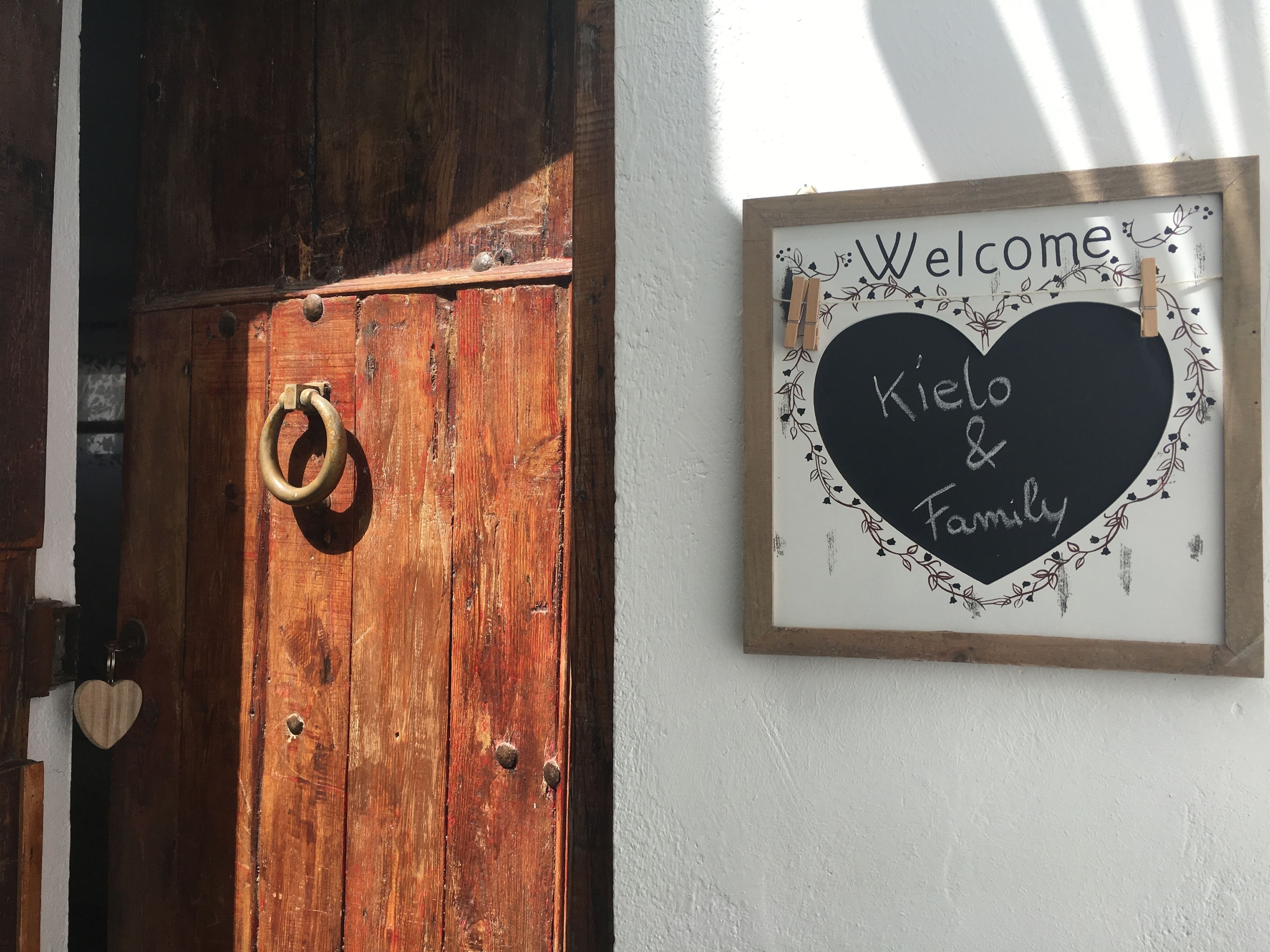 Eine Holztür mit einem Messing-Ringgriff und einem herzförmigen Schild mit der Aufschrift 'Welcome Kielo & Family'.
