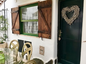 Uma casa rústica com porta verde, uma grinalda em formato de coração e uma janela com persianas de madeira.