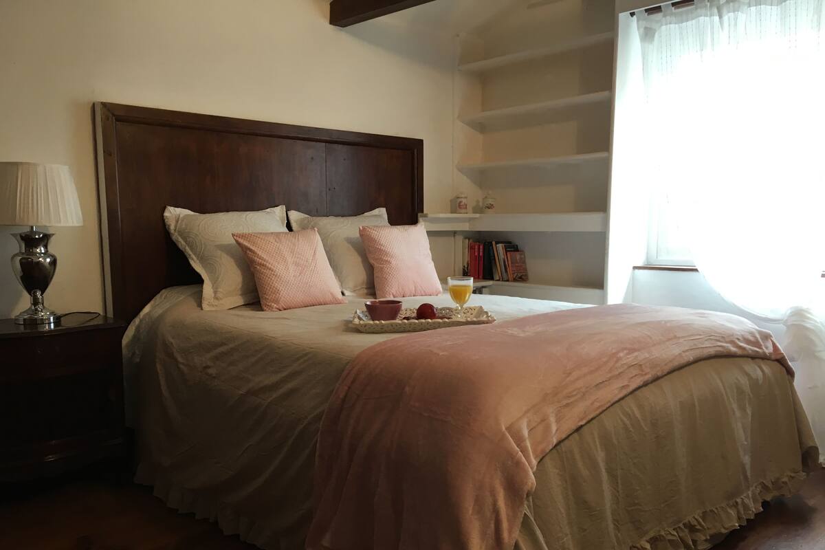 A neatly made bed with a wooden headboard, a bedside table with a lamp, and a tray with a drink and fruit.
