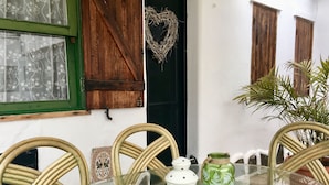 A dining area with a glass table, wicker chairs, and decorative items including a green jar with white fern designs, a white lantern, and a heart-shaped wreath. - La Casita de Las Palmas VV (Las Palmas de Gran Canaria)