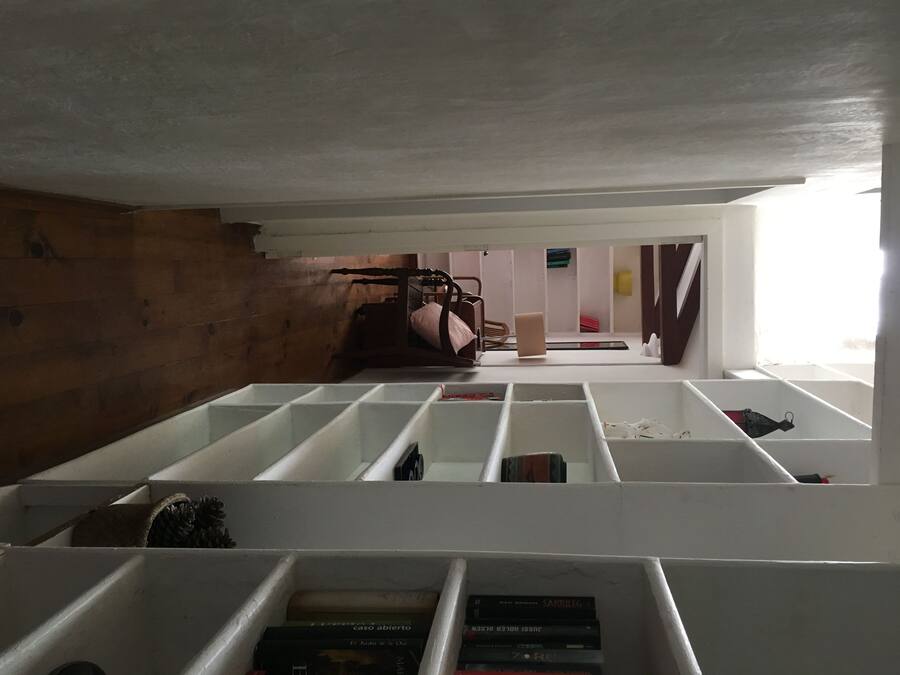 Una habitación con cama alta, pared de madera y estantería blanca con libros.